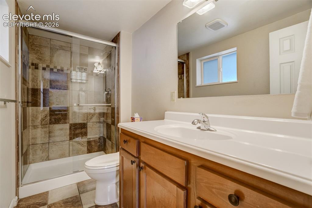 Image 31 of 50: Glass-enclosed shower with checkered tile surround, wood-finish vanity with
