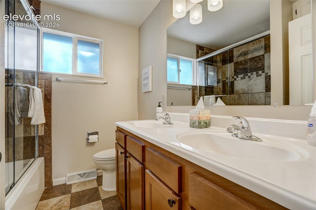 Image 32 of 50: Dual sink vanity with wood-finish cabinetry, a large mirror, and overhead v