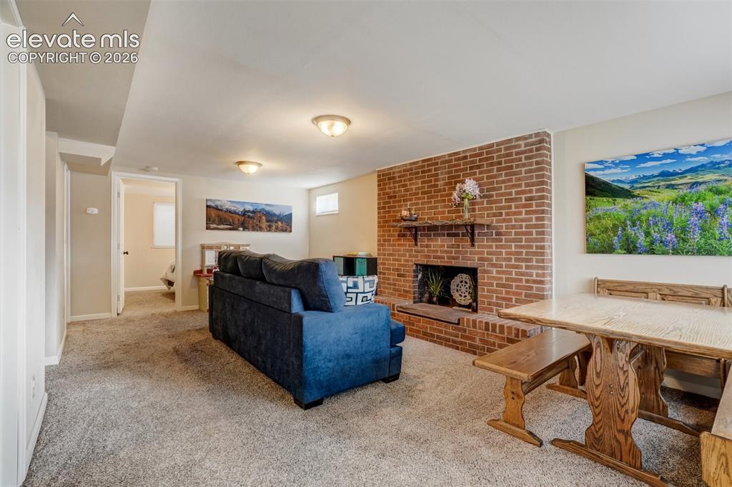 Image 35 of 50: Brick fireplace with hearth, carpeted flooring, and built-in ceiling lighti