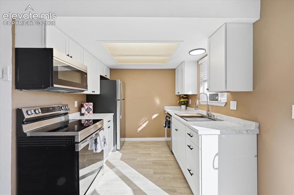 Image 12 of 27: White cabinetry, stainless steel appliances, light-toned wood-finish floori