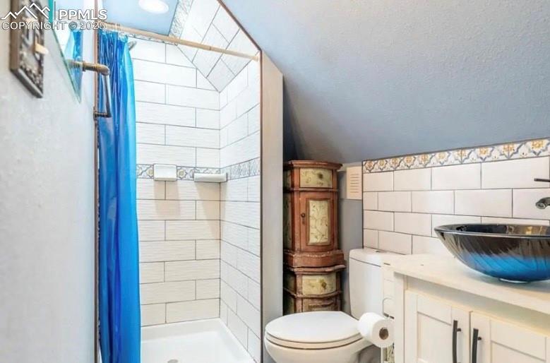 Image 5 of 9: Bathroom with lofted ceiling, a shower stall, vanity, and tile walls