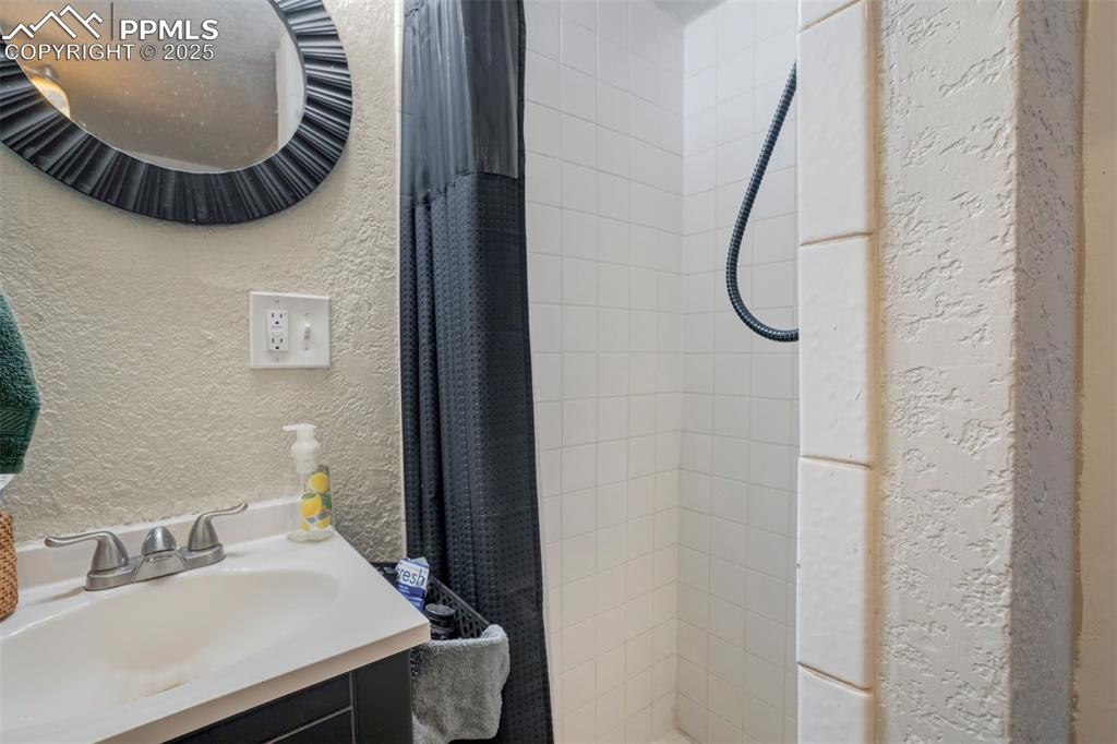 Image 19 of 24: Full bath with a textured wall, a tile shower, and vanity