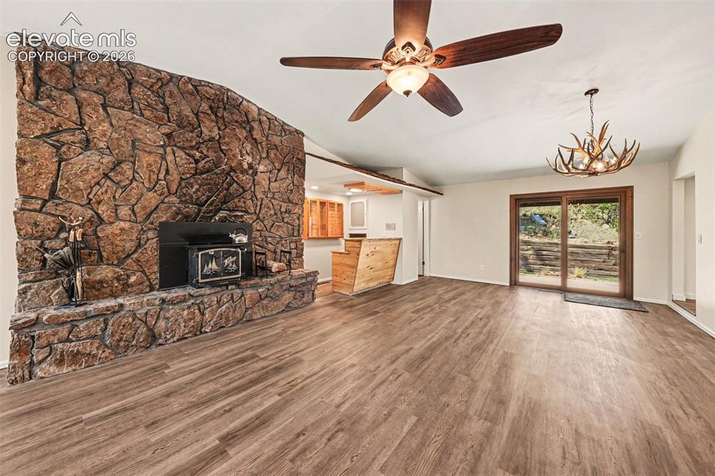 Image 12 of 42: Spacious room featuring a prominent stone fireplace with a wood-burning sto