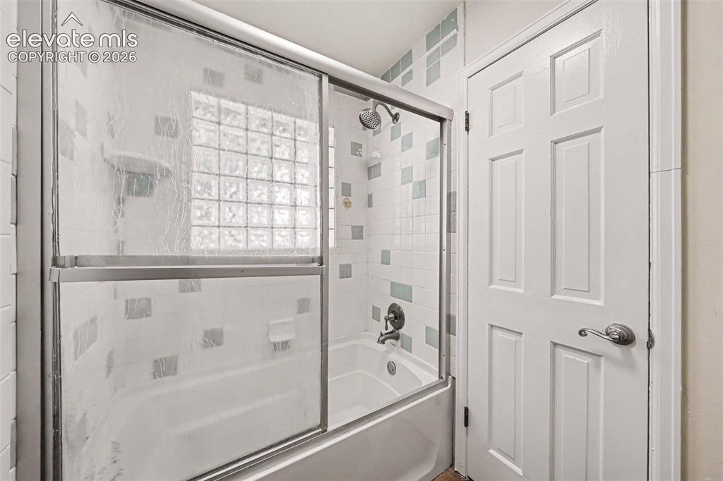 Image 19 of 42: Bathtub with sliding glass enclosure, mosaic-patterned tile surround, glass