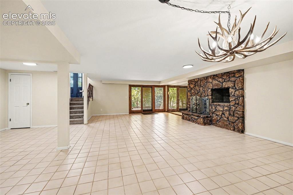 Image 22 of 42: Spacious lower level featuring light-toned tile flooring, a stone-clad fire