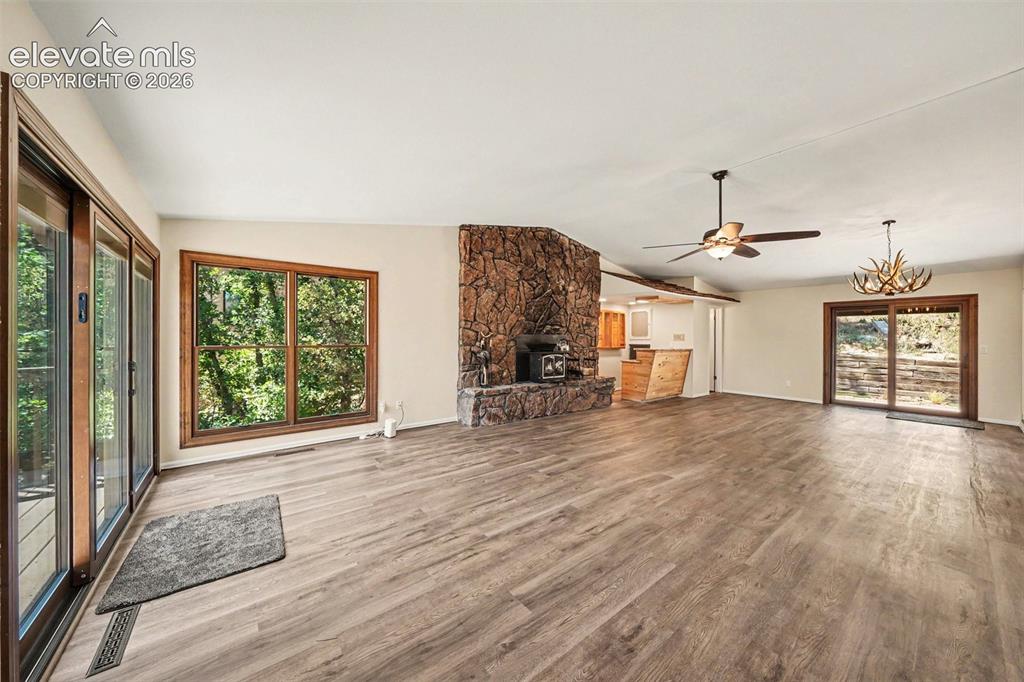Image 8 of 42: Spacious living area featuring wood-finish flooring, a stone fireplace, and