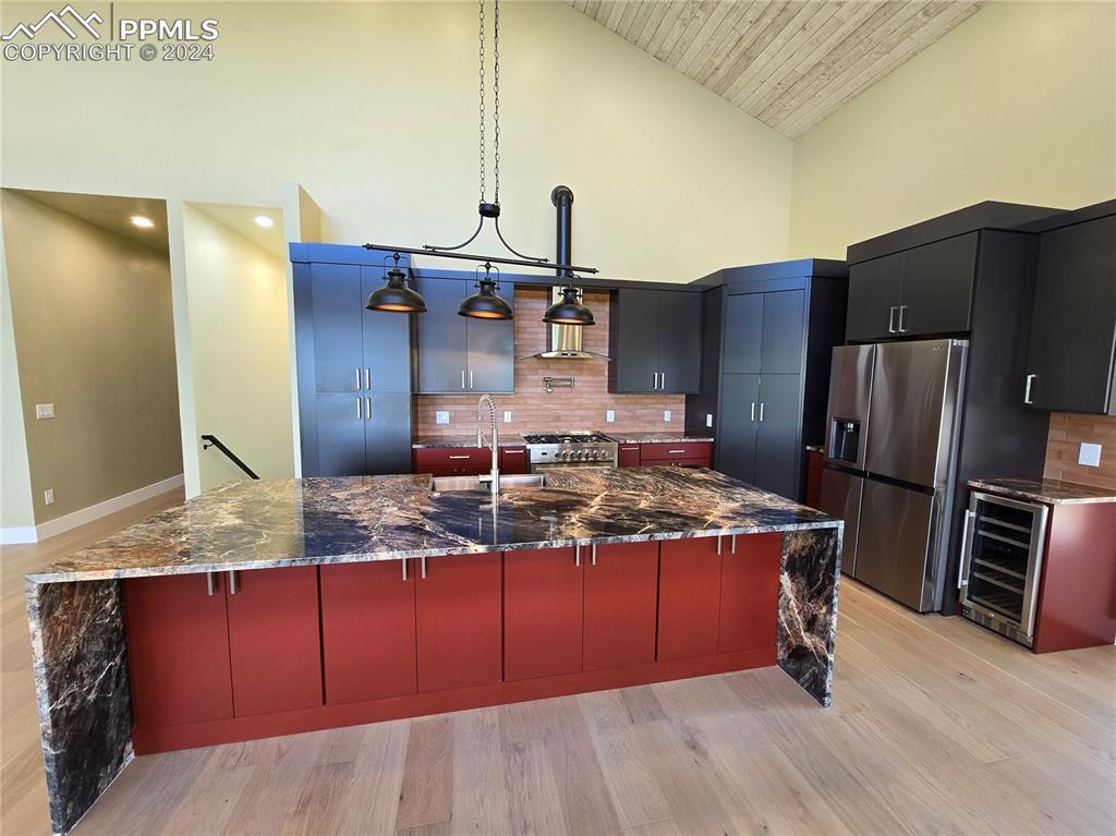 Image 18 of 50: Kitchen featuring a large island with sink, backsplash, wine cooler, hangin