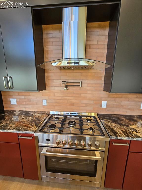 Image 23 of 50: Kitchen featuring dark stone countertops, exhaust hood, decorative backspla