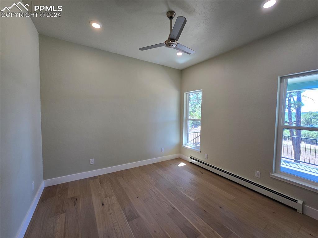 Image 30 of 50: Primary bedroom with a baseboard heating unit, ceiling fan, and light hardw