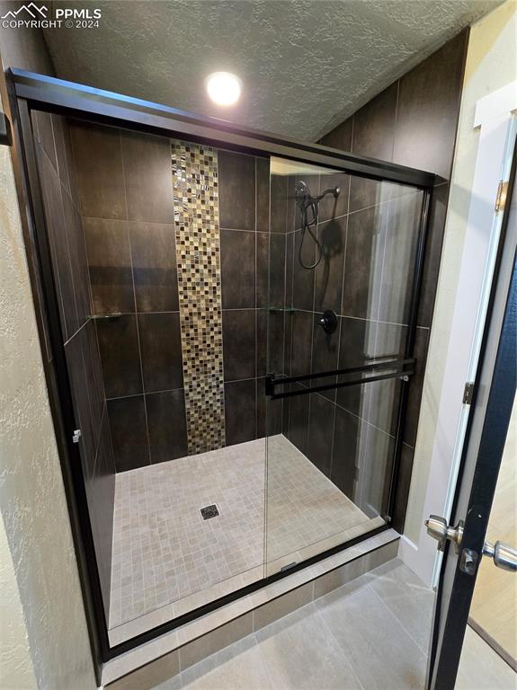 Image 37 of 50: Bathroom with a shower with door, tile patterned floors, and a textured cei