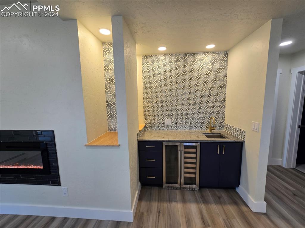 Image 40 of 50: Bar with a textured ceiling, backsplash, wine cooler, sink, and dark hardwo