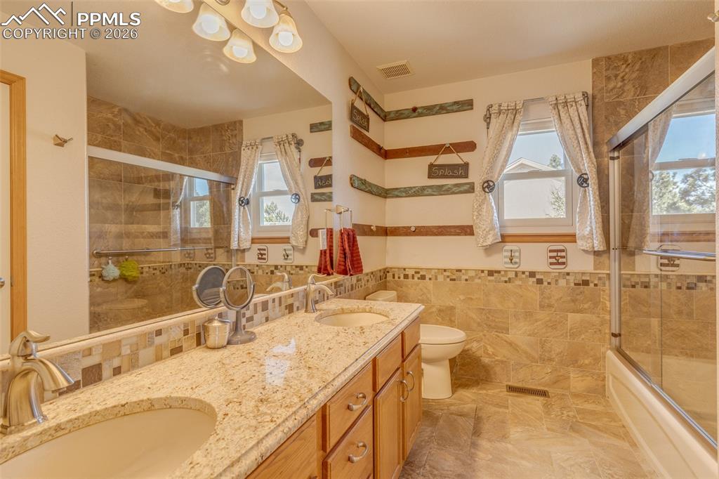 Image 35 of 48: Full bath with double vanity, enclosed tub / shower combo, and tile walls