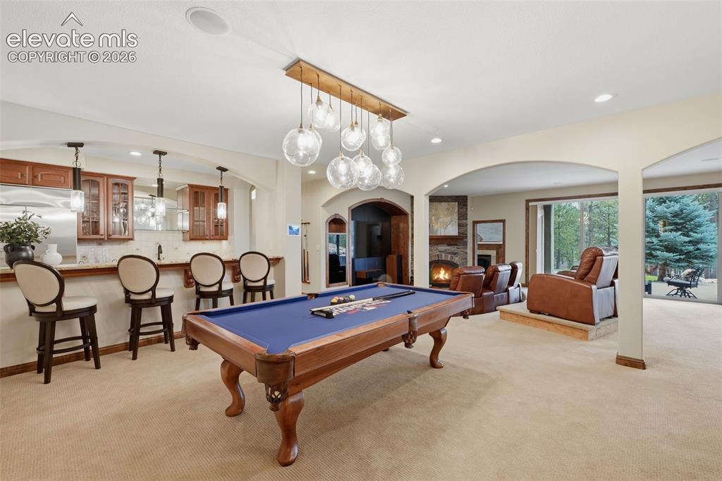 Image 27 of 50: Entertainment area in the basement with wet bar, movie area, fireplace, win