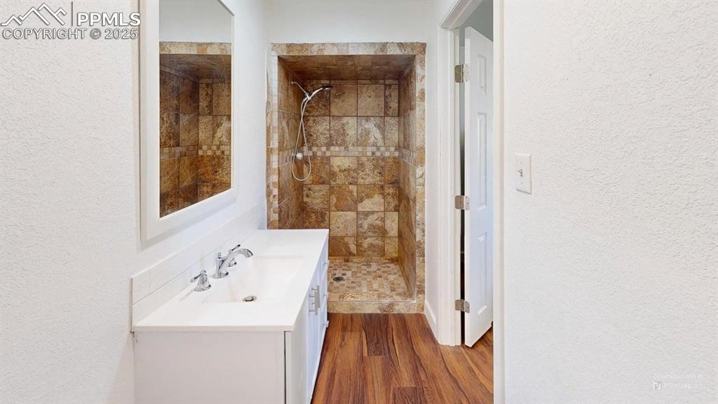 Image 13 of 27: Full bath with a tile shower, a textured wall, and vanity