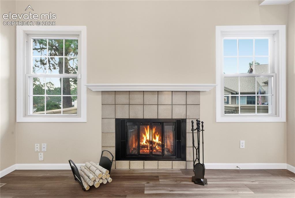 Image 12 of 35: Fireplace with a tile surround and mantel, flanked by two windows