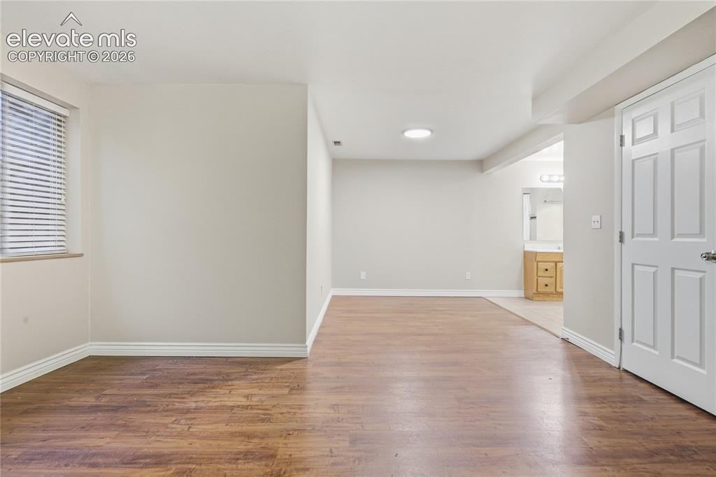 Image 29 of 35: Spacious room featuring wood-finish flooring, a window with blinds, and whi