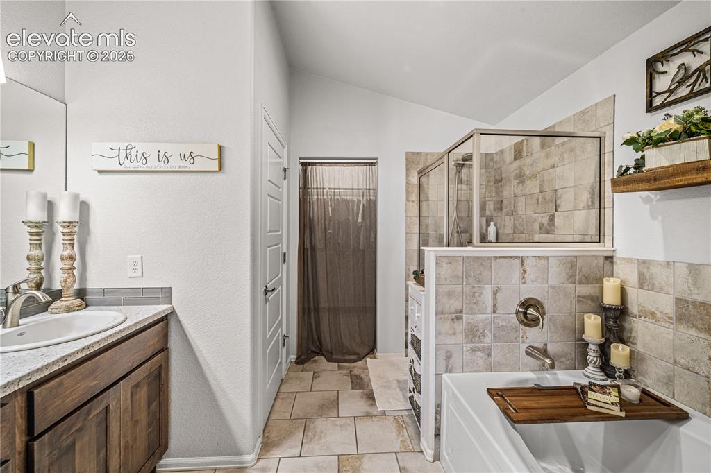 Image 18 of 50: Bathroom featuring a soaking tub, glass-enclosed shower, wood-finish vanity