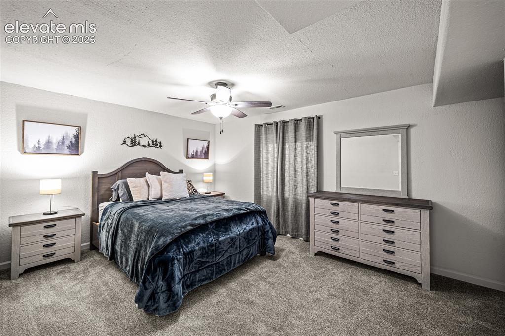 Image 38 of 50: Carpeted bedroom with a ceiling fan, a window with curtains, and wall-mount