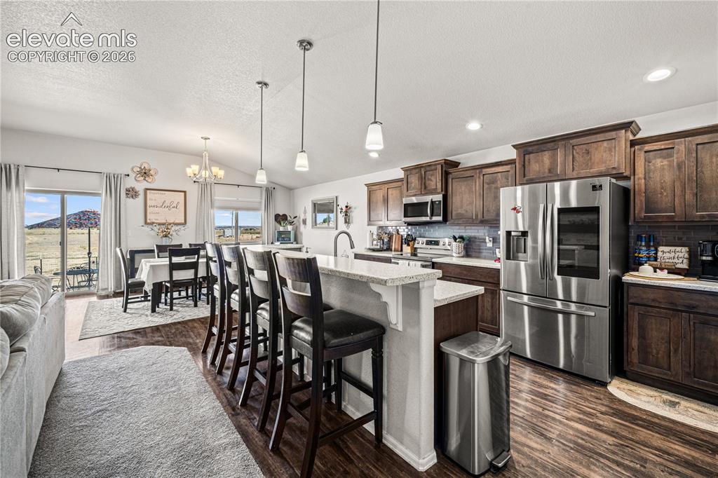 Image 6 of 50: Kitchen and dining area featuring wood-finish flooring, vaulted ceilings, a