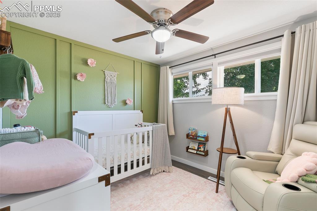 Image 16 of 37: Bedroom featuring a crib, light wood finished floors, ceiling fan, and a de