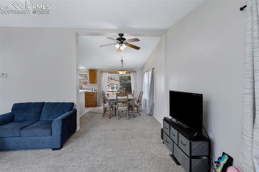 Image 7 of 24: Living room with light colored carpet, vaulted ceiling, and a ceiling fan