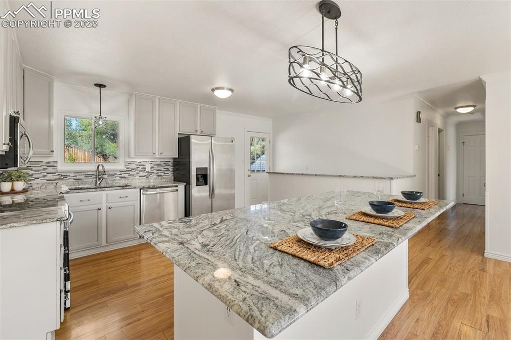 Image 18 of 47: Kitchen with hanging light fixtures, light stone counters, decorative backs