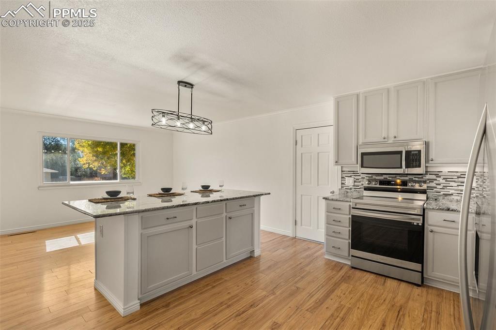Image 21 of 47: Kitchen with stainless steel appliances, light stone countertops, hanging l