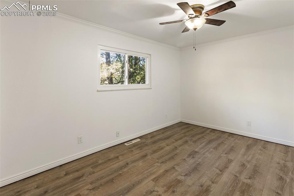 Image 35 of 47: Empty room with crown molding, dark wood finished floors, and a ceiling fan