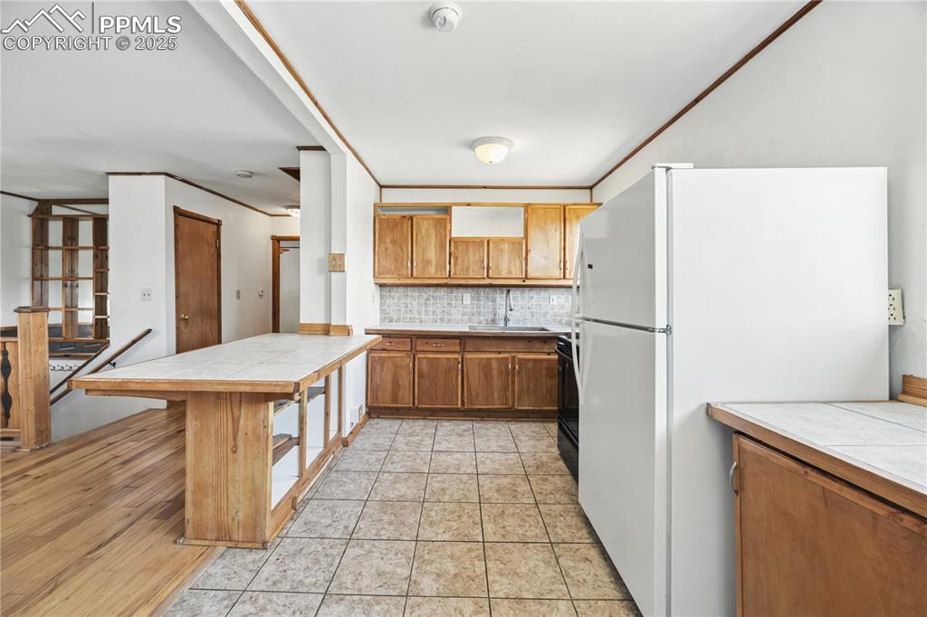 Image 10 of 23: Kitchen featuring tile countertops, crown molding, freestanding refrigerato
