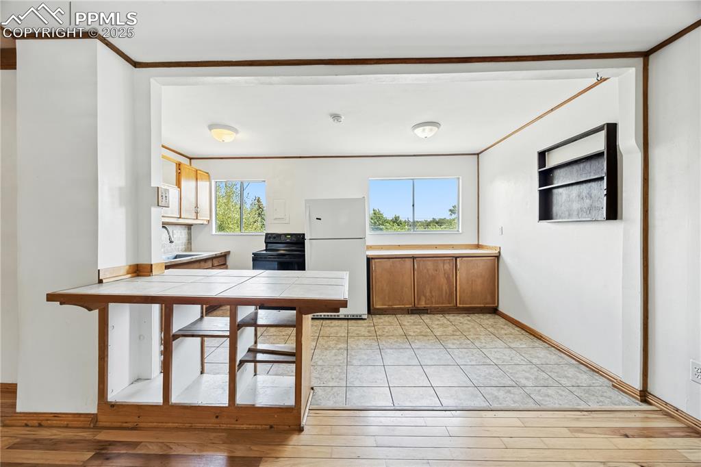 Image 8 of 23: Kitchen with brown cabinets, freestanding refrigerator, tile countertops, l