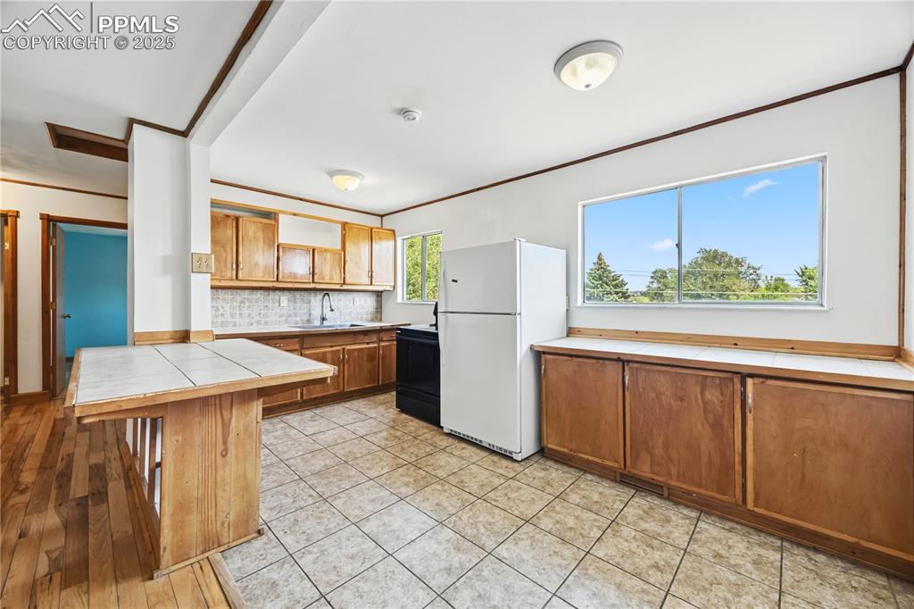 Image 9 of 23: Kitchen with brown cabinetry, tile counters, crown molding, a breakfast bar