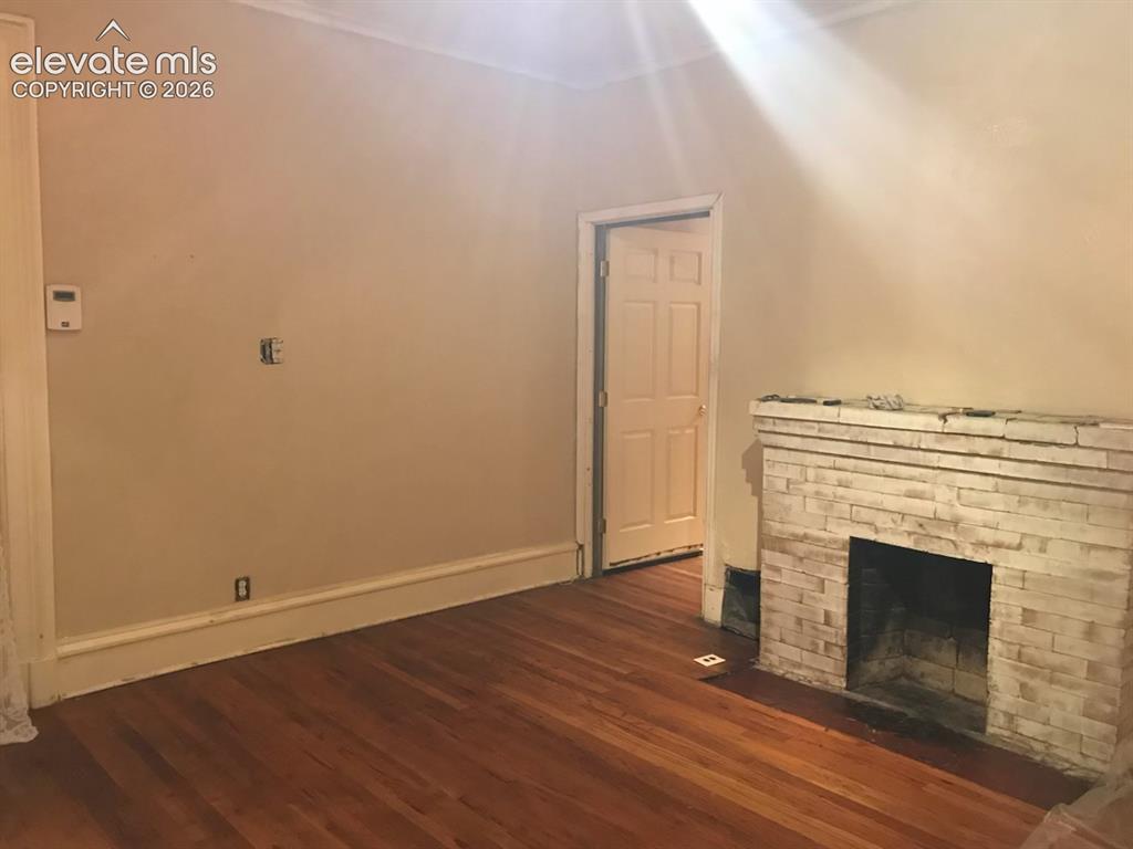 Image 19 of 27: Hardwood flooring, crown molding, and a brick-finish fireplace