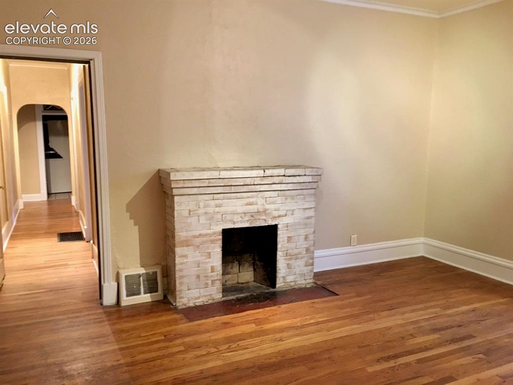 Image 4 of 27: Brick fireplace with a stone mantel, wood-finish flooring, and crown moldin