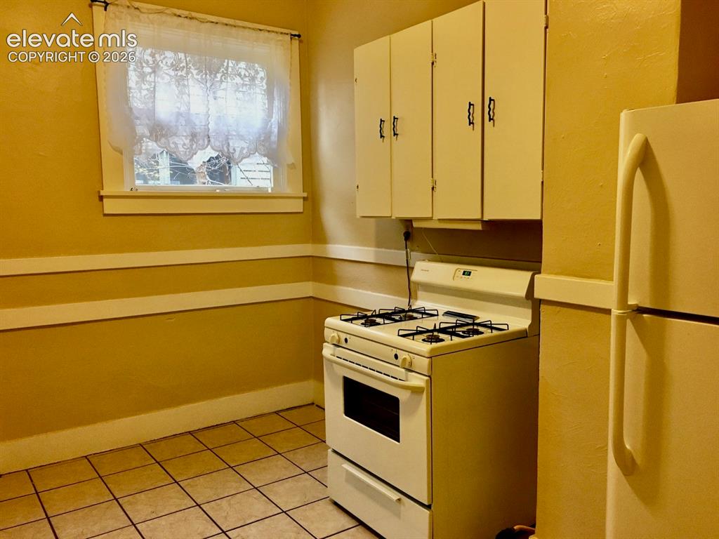 Image 5 of 27: Window with trim, upper cabinetry, gas range, refrigerator, and tile floori