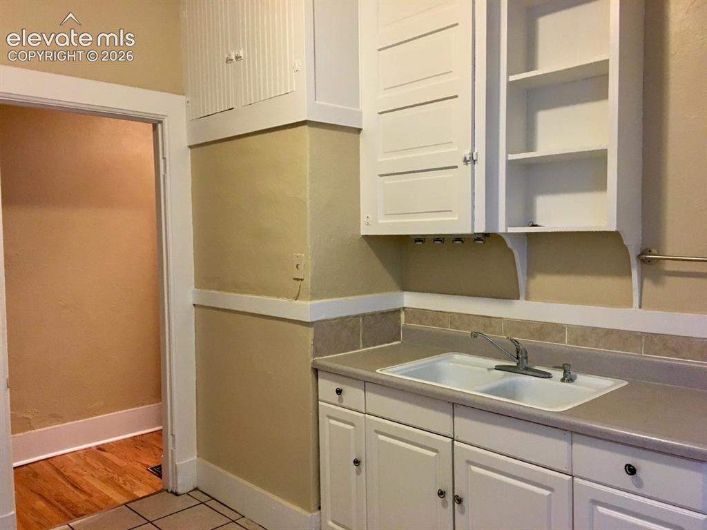 Image 6 of 27: White cabinetry with paneled doors and open shelving, dual-basin sink with