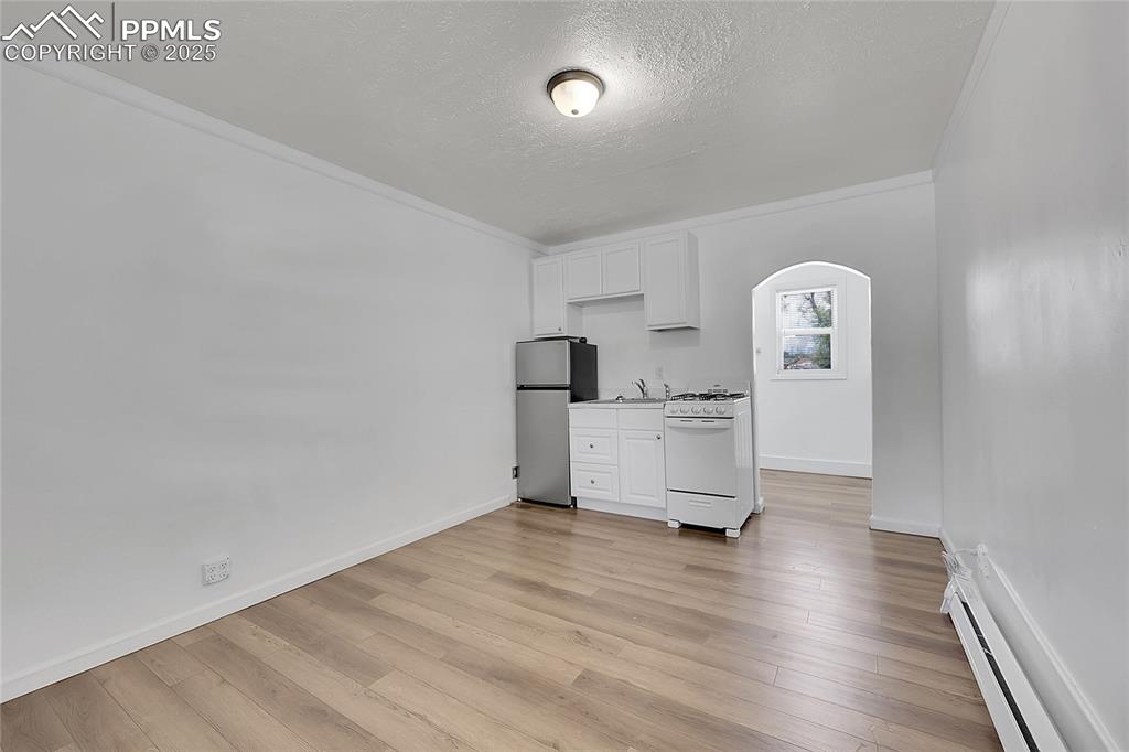 Image 20 of 32: Unfurnished living room featuring baseboard heating, arched walkways, a tex