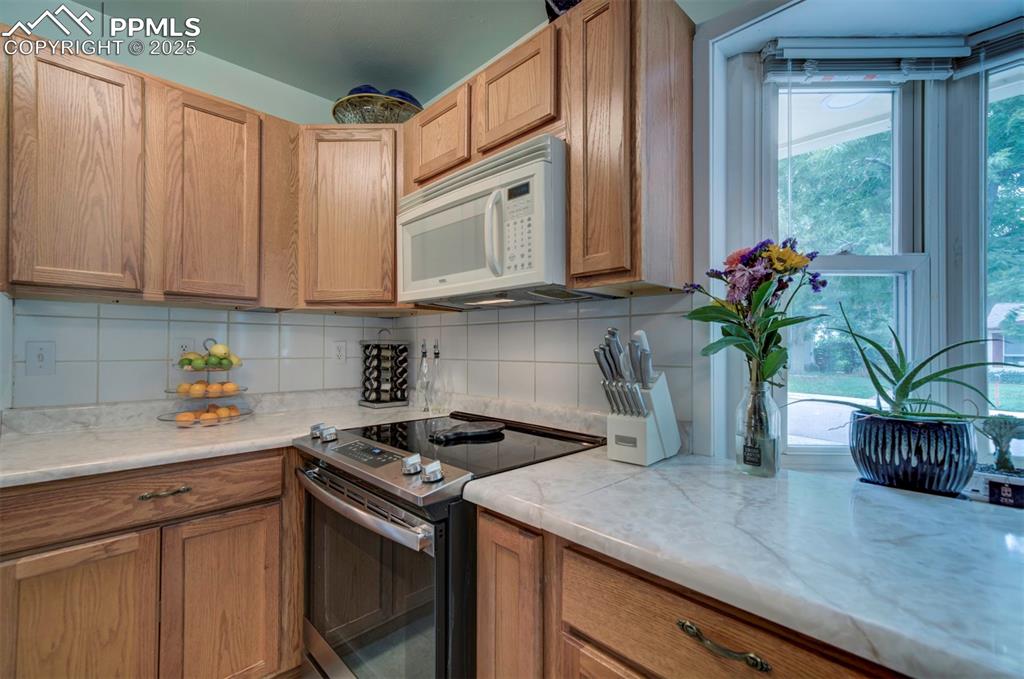 Image 10 of 32: Kitchen with electric stove, decorative backsplash, white microwave, and li