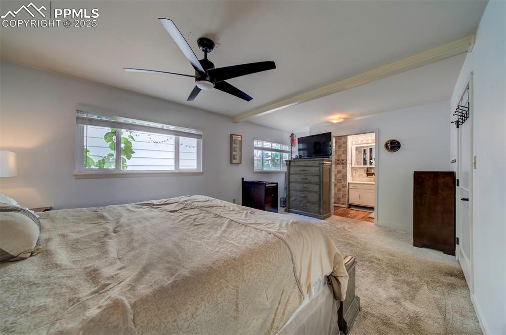 Image 16 of 32: Carpeted bedroom featuring connected bathroom, ceiling fan, and beamed ceil