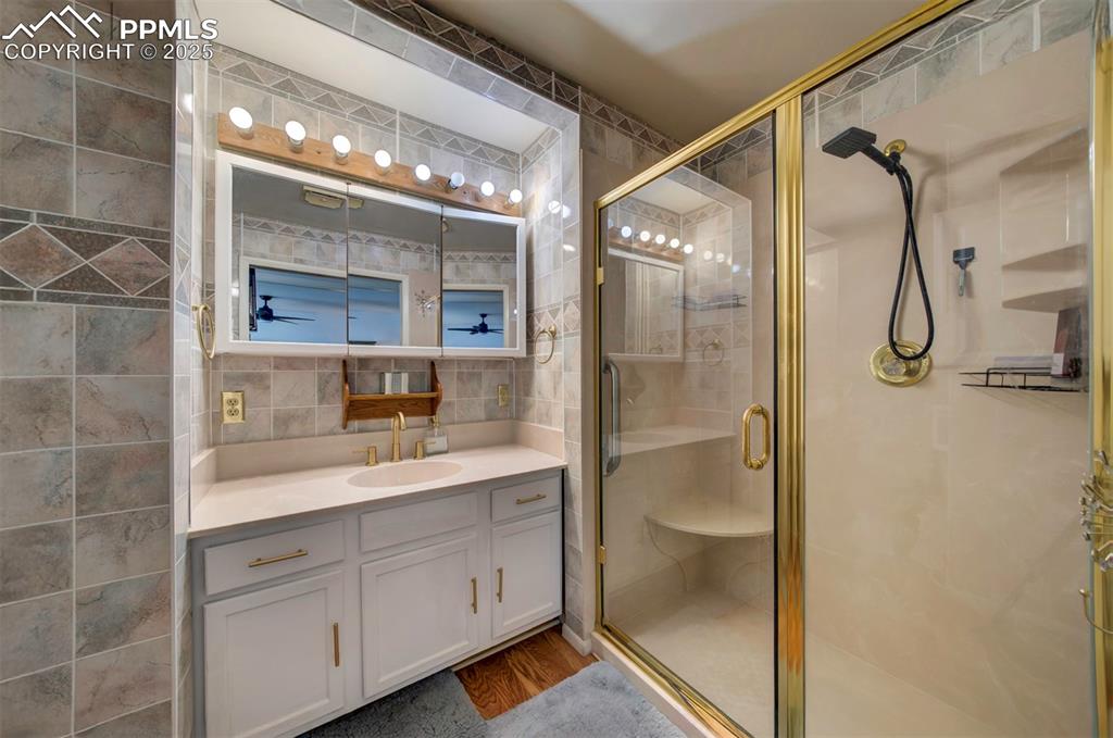 Image 18 of 32: Full bath with tile walls, vanity, a stall shower, and backsplash
