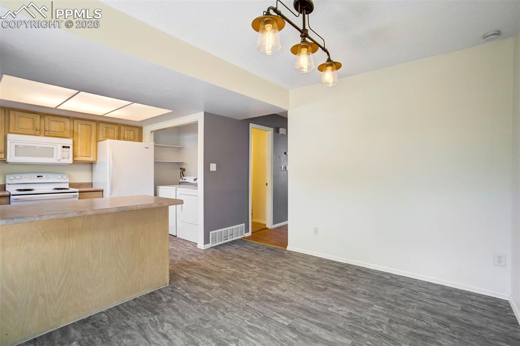 Image 11 of 49: Kitchen featuring wood cabinetry, white appliances, and a breakfast bar wit