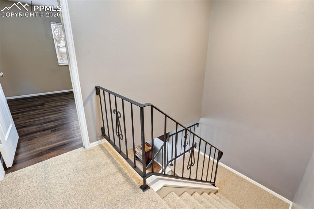 Image 14 of 49: Staircase featuring a wrought iron railing, neutral carpet, and white trim
