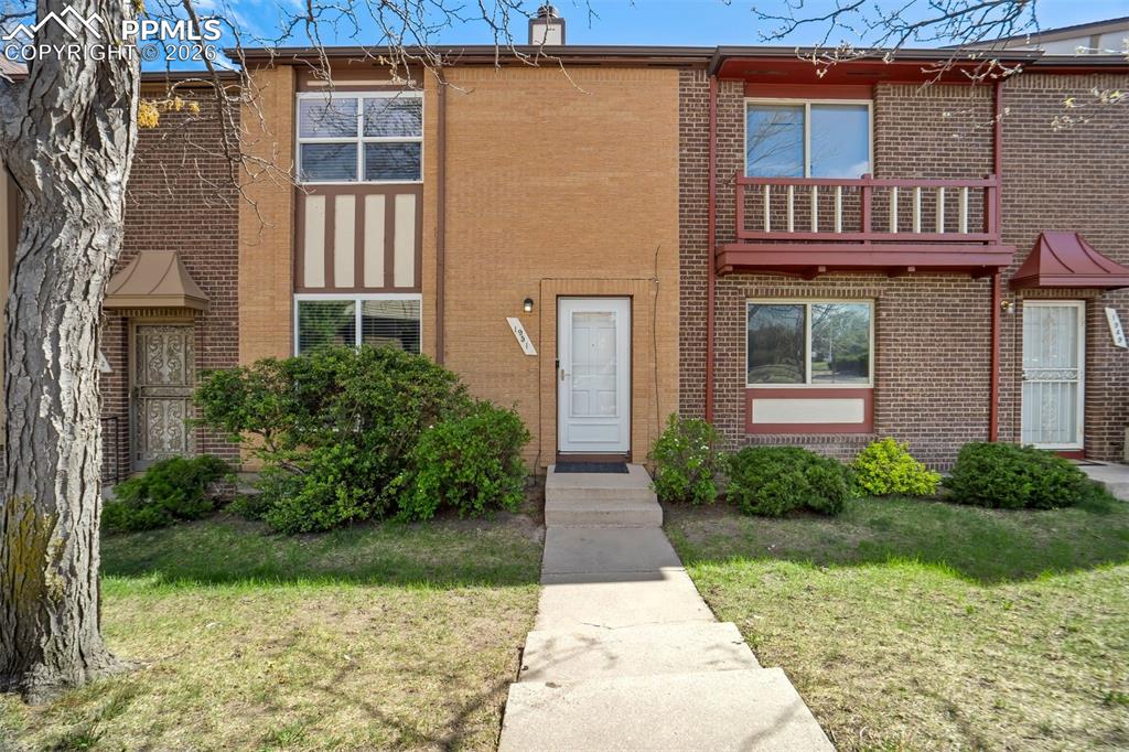 Image 2 of 49: Brick exterior featuring a concrete walkway, mature shrubs, and a second-st