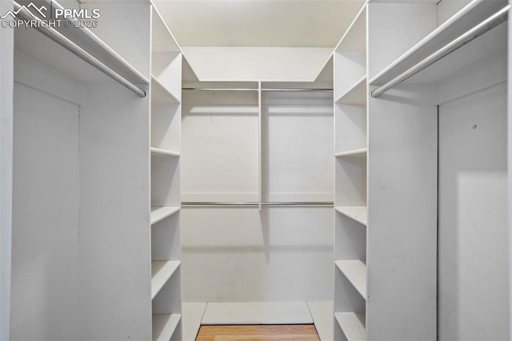 Image 26 of 49: Spacious walk-in closet featuring white built-in shelving, multiple hanging