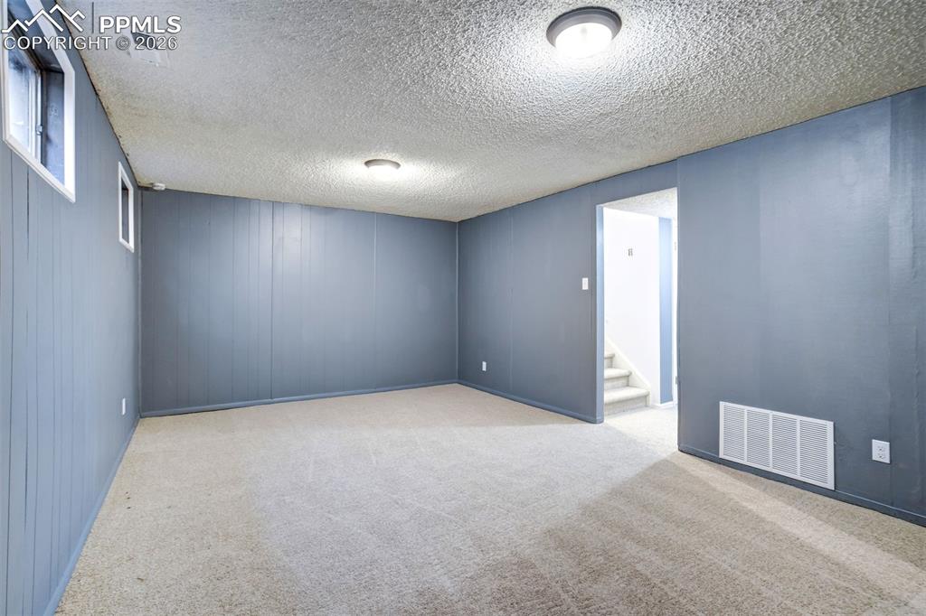Image 28 of 49: Carpeted room featuring blue paneled walls and a textured ceiling