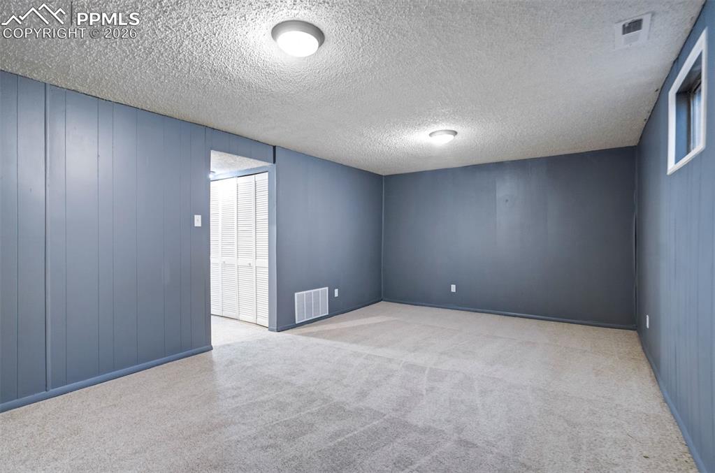 Image 34 of 49: Spacious room featuring light gray carpeting, blue-gray paneled walls, and 