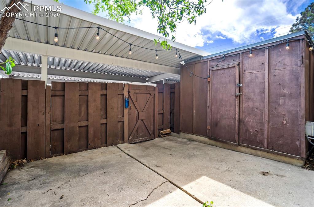 Image 38 of 49: Covered patio area featuring string lighting, concrete flooring, a privacy 