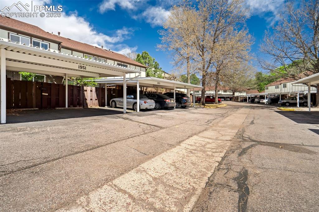 Image 40 of 49: Covered parking spaces with white metal carports and an asphalt drive