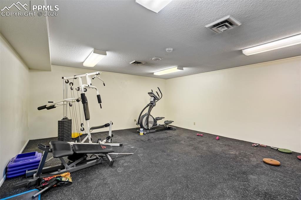 Image 49 of 49: Spacious room with dark rubber flooring, white painted walls, and overhead 