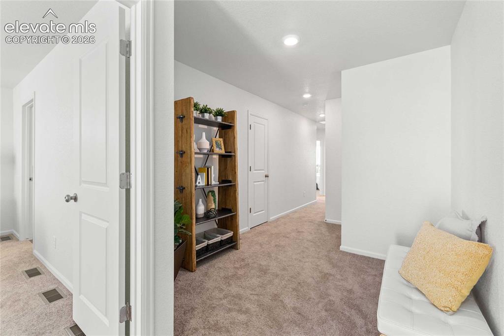 Image 11 of 30: Recessed lighting illuminates the carpeted hallway with white walls and tri