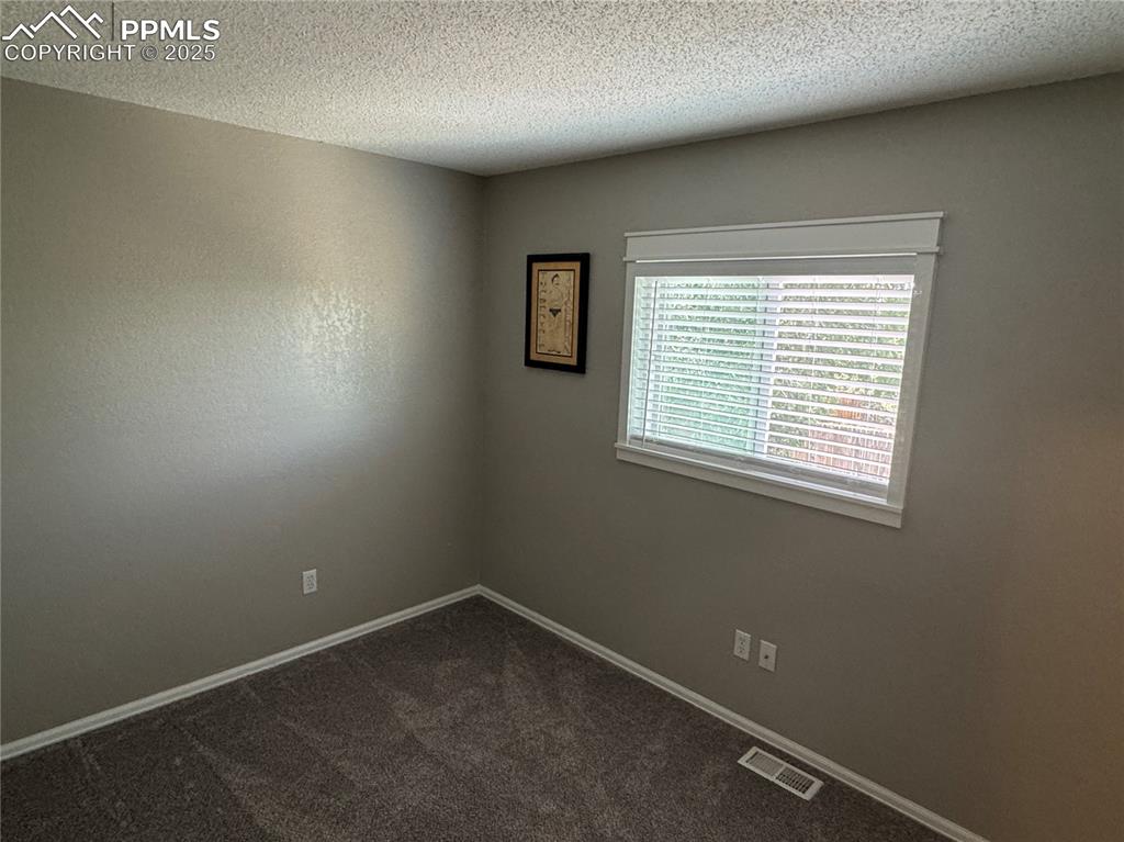 Image 13 of 40: Spare room with a textured ceiling and dark colored carpet